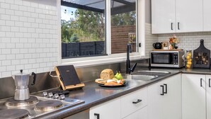 Een moderne keuken met witte kastjes, roestvrijstalen apparatuur en een groot raam met uitzicht op groen.