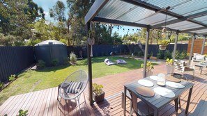 Een overdekte patio met een houten terras, tuinmeubilair en een tuin met gazon en bomen.