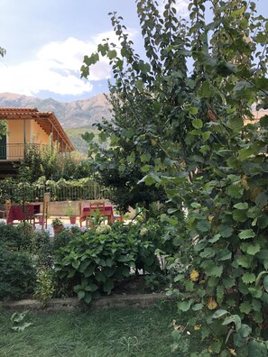 A garden with a patio area, a building with a tiled roof, and mountains in the background.