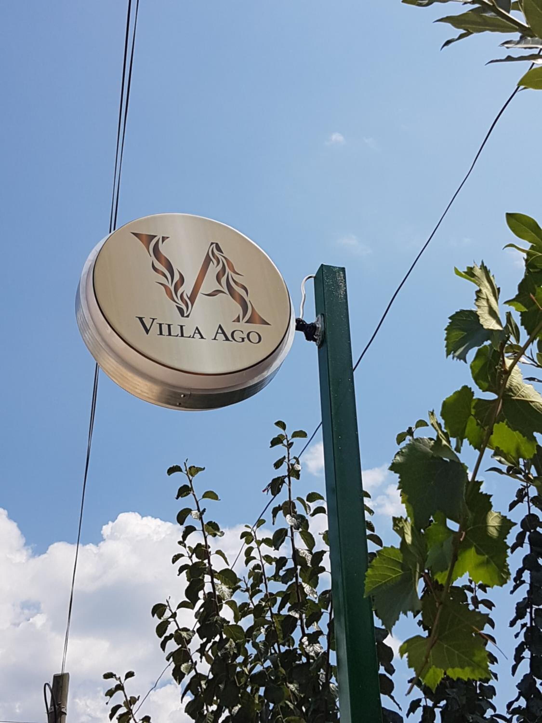 A circular sign with the text "Villa Ago" and a stylized flame design.