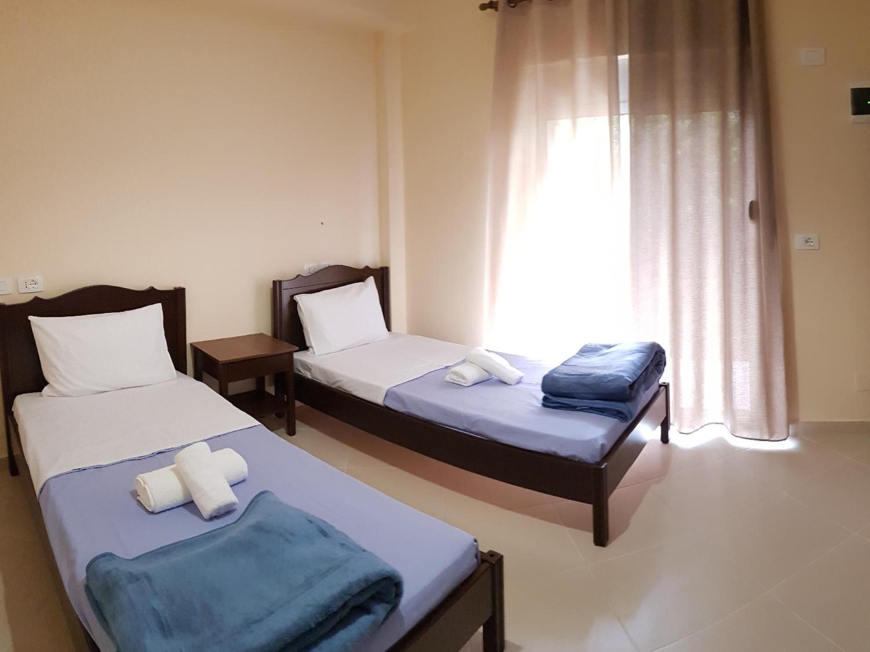 Habitación de hotel con dos camas individuales, una mesita y un ventanal con cortinas.