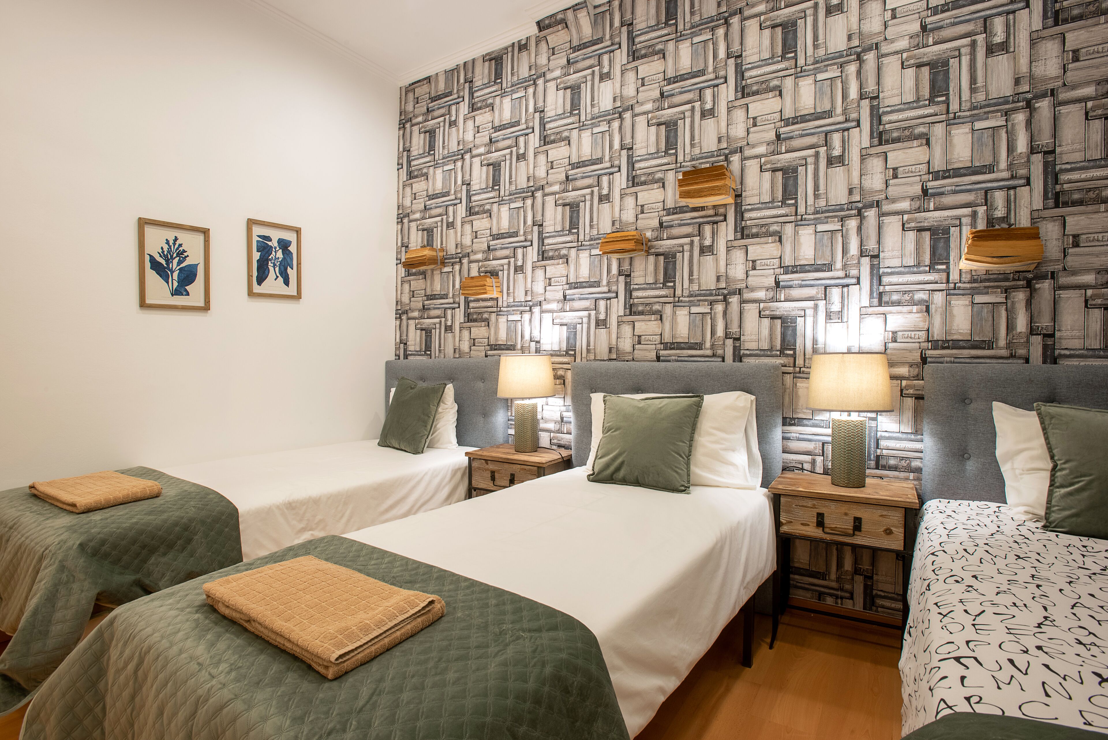 A hotel room with two beds, a patterned wall, and two framed pictures.
