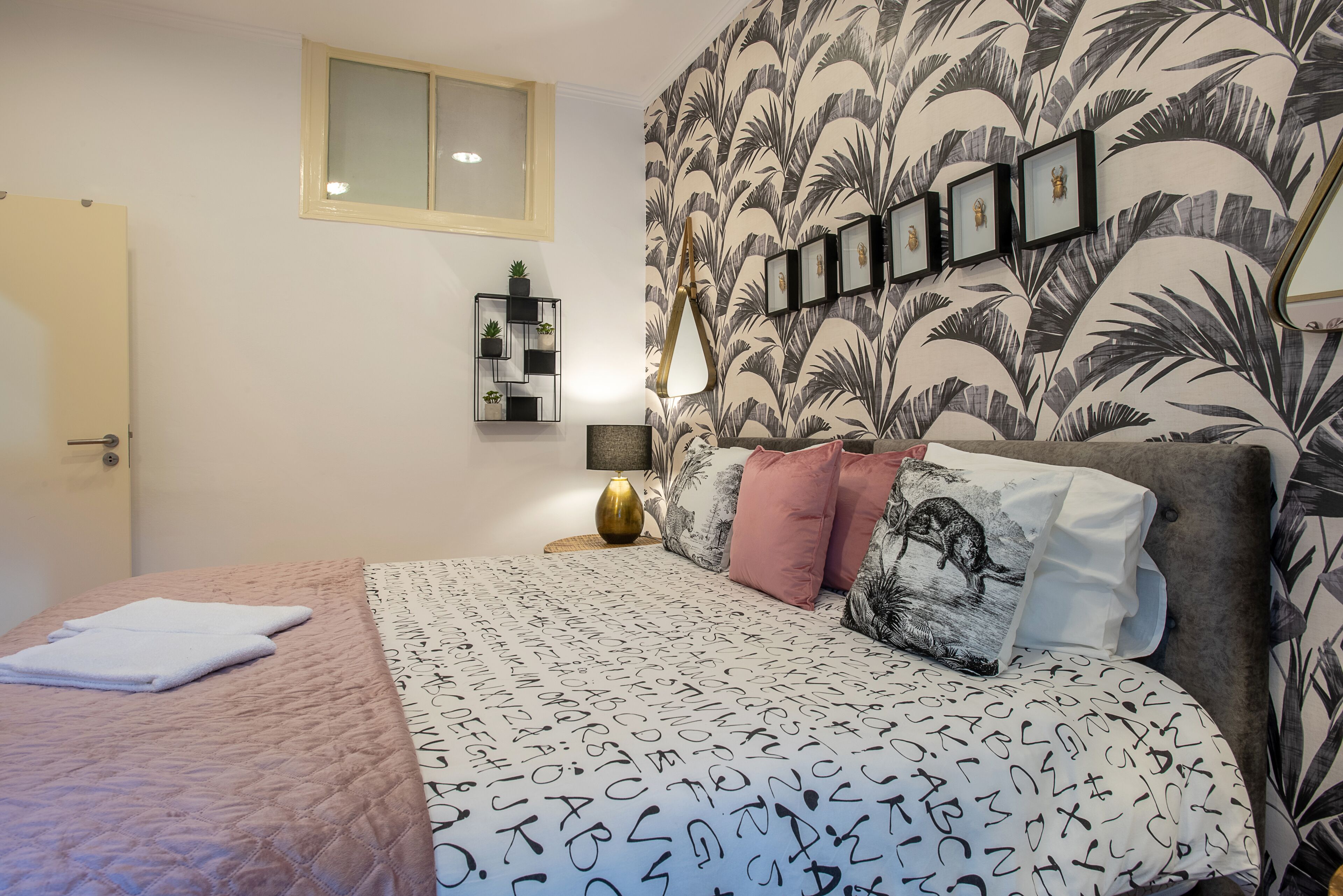Une chambre à coucher avec un lit, une table de chevet, une fenêtre et un mur orné de tableaux.