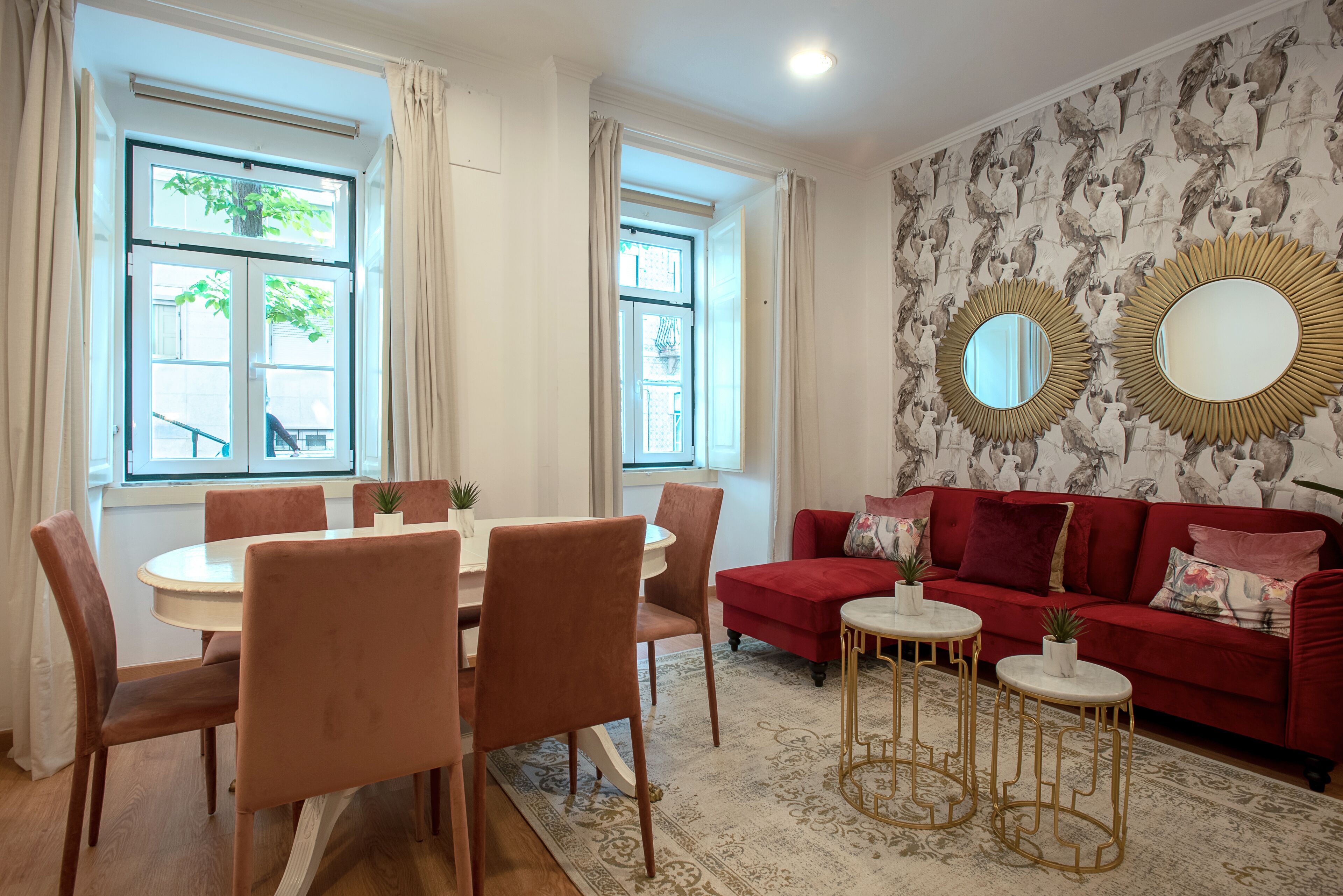 Un comedor con una mesa redonda y sillas, un sofá rojo y espejos decorativos en la pared.