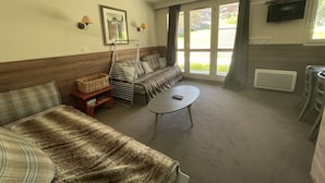 A cozy room with a sofa, a small table, a wicker basket, a metal drying rack, and a TV mounted on the wall. - La Valériane 10 - Beautiful 3 room apartment, beautiful view on the mountain (LES AVANCHERS VALMOREL)