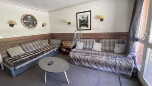 A cozy living room with a sofa, a small round table, and a wall clock. - La Valériane 10 - Beautiful 3 room apartment, beautiful view on the mountain (LES AVANCHERS VALMOREL)