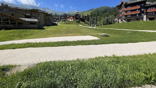 A view of a mountain town with buildings, a gravel path, and a grassy area. - La Valériane 10 - Beautiful 3 room apartment, beautiful view on the mountain (LES AVANCHERS VALMOREL)