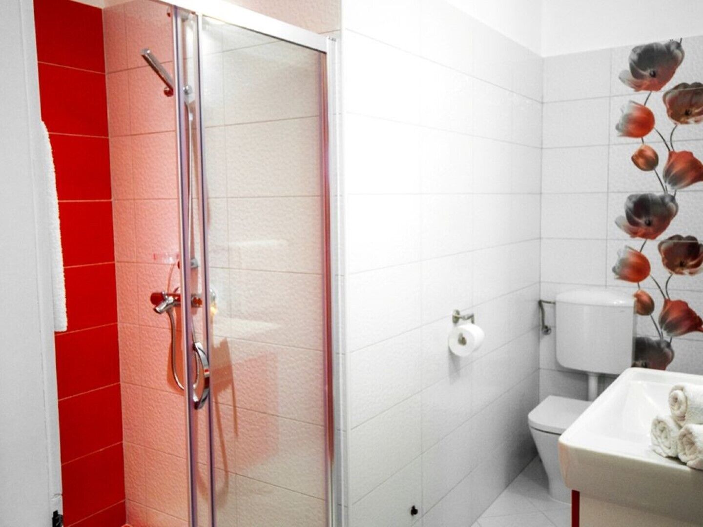 A bathroom with a glass shower enclosure, a toilet, and a sink with a towel.