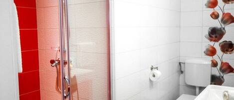 A bathroom with a glass shower enclosure, a toilet, and a sink with a towel.