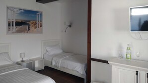 Une chambre d’hôtel avec deux lits, une télévision, une petite armoire et un tableau représentant une scène de plage.