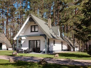 A two-story house with a sloped roof, a covered porch, and a large window. - 55m²- DHH (a) - Cottages by the lake (Nossentiner Hütte)