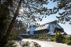 A snow-covered building with a traditional architectural style, surrounded by trees and a clear sky. - 55m²- DHH (a) - Cottages by the lake (Nossentiner Hütte)