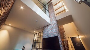 A modern interior with a brick fireplace, a glass railing, and a staircase leading to an upper level. - Hotel March (Daejeon)