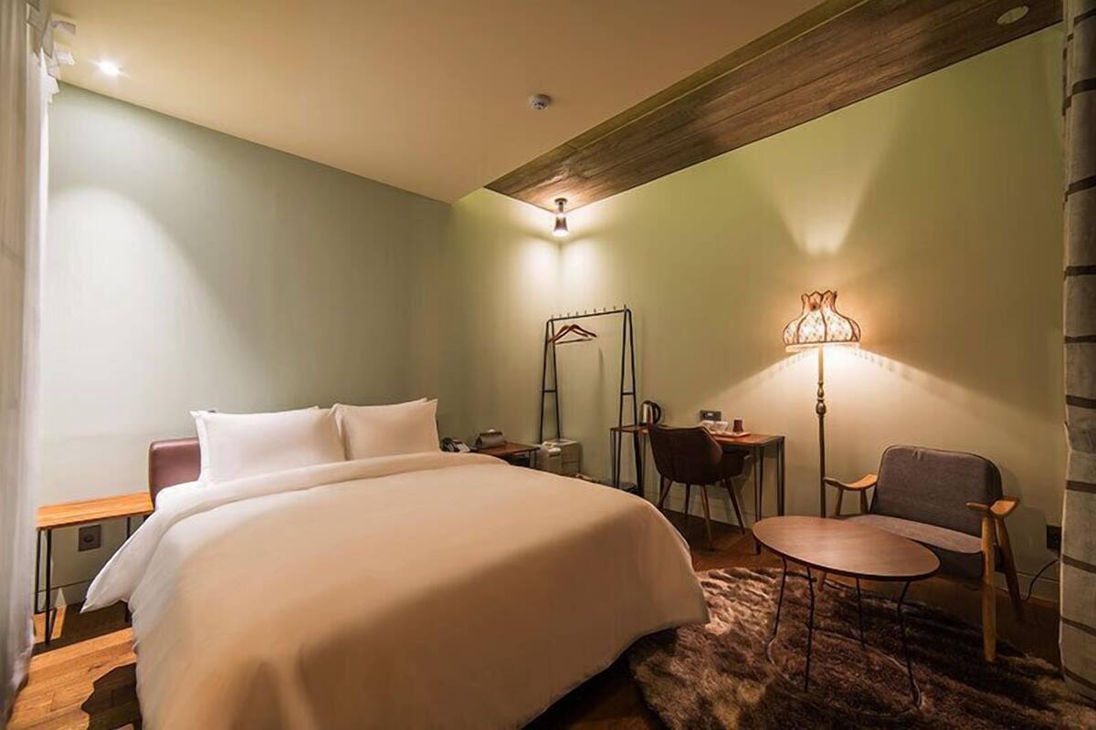 A hotel room with a large bed, a desk with a chair, a lamp, and a mirror.