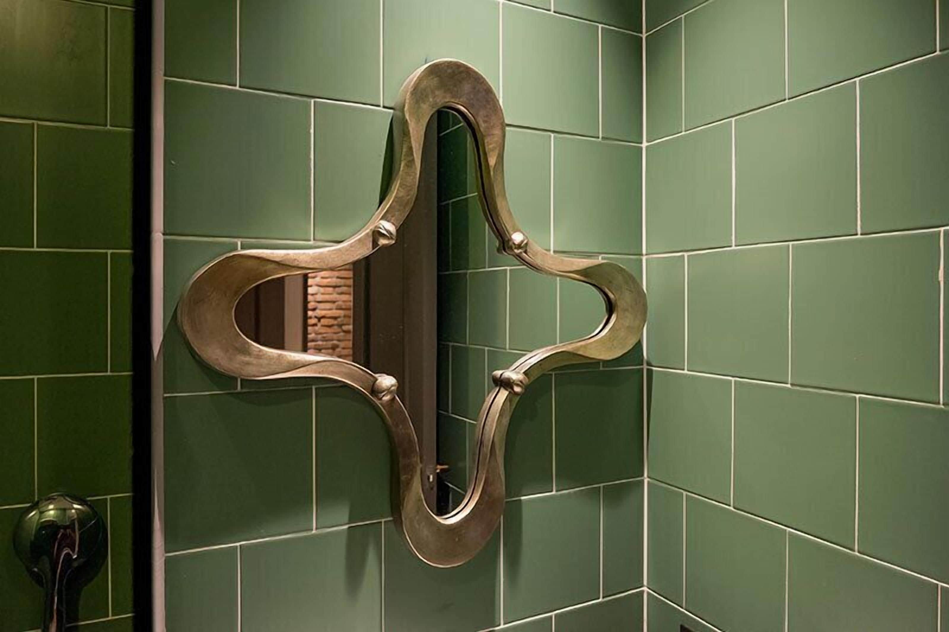 Espejo con un marco decorativo sobre una pared con azulejos verdes.