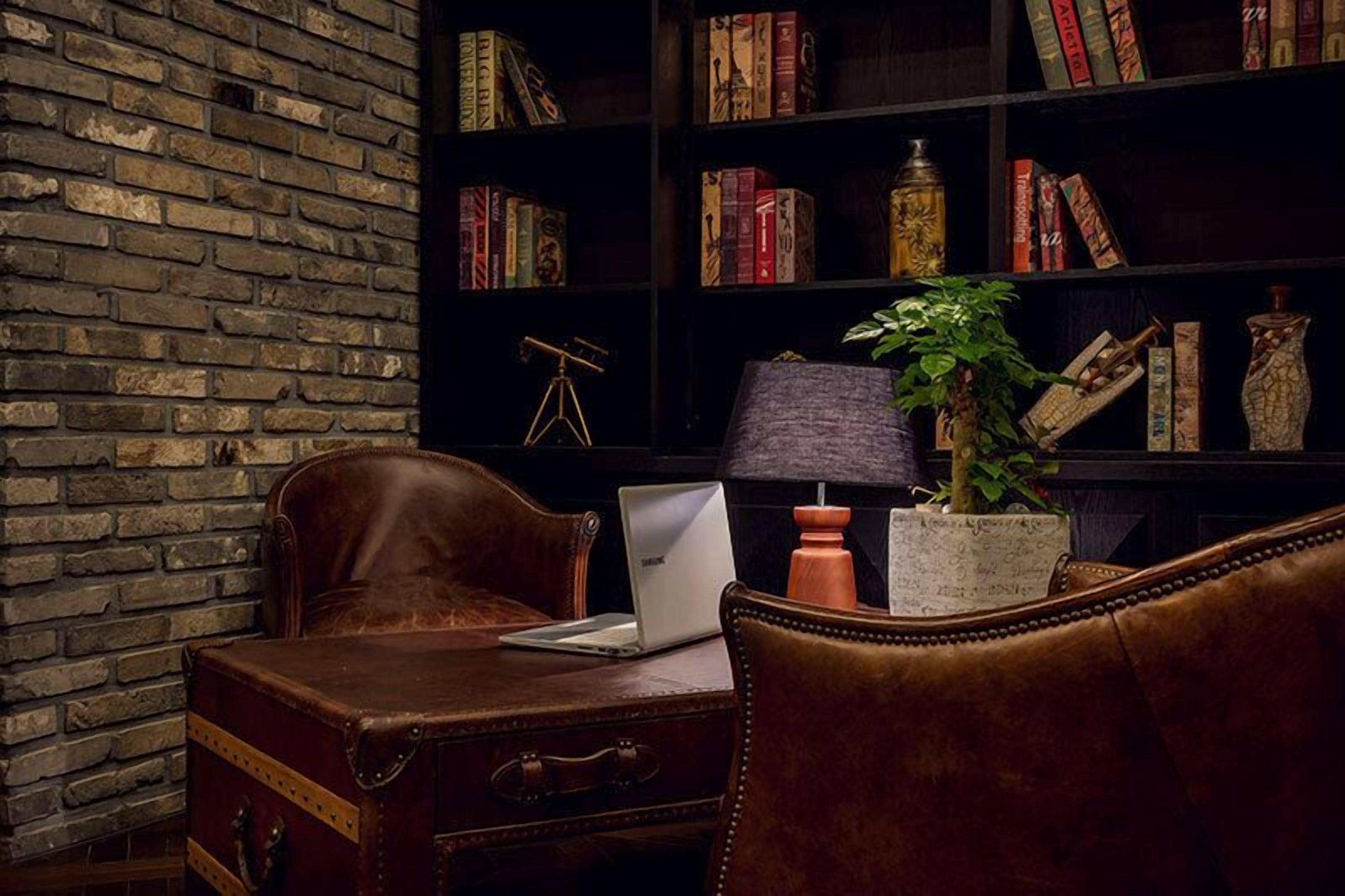 A cozy reading nook with a leather armchair, a wooden desk with a laptop, a bookshelf filled with books, and a vintage telescope.