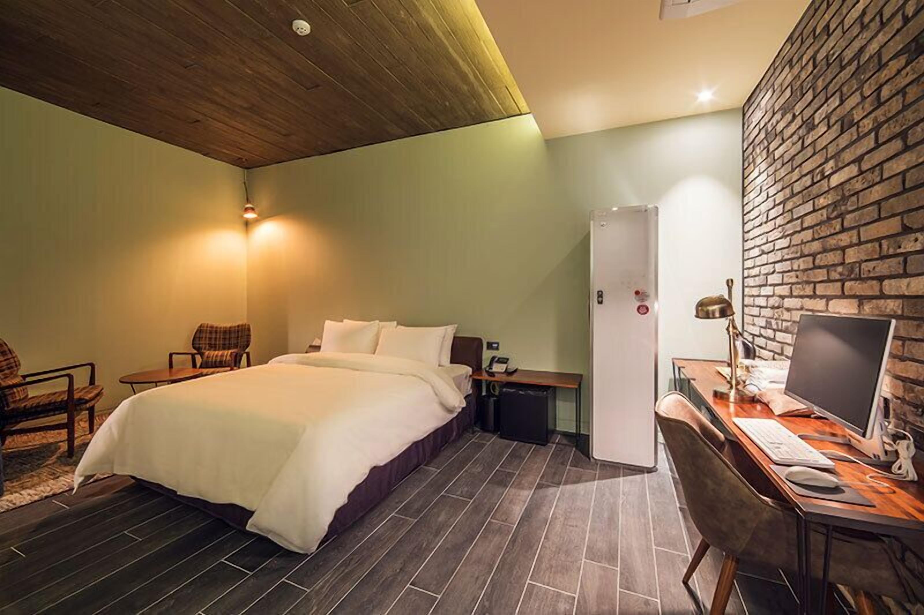 A hotel room with a bed, a desk with a computer, a chair, and a small table.