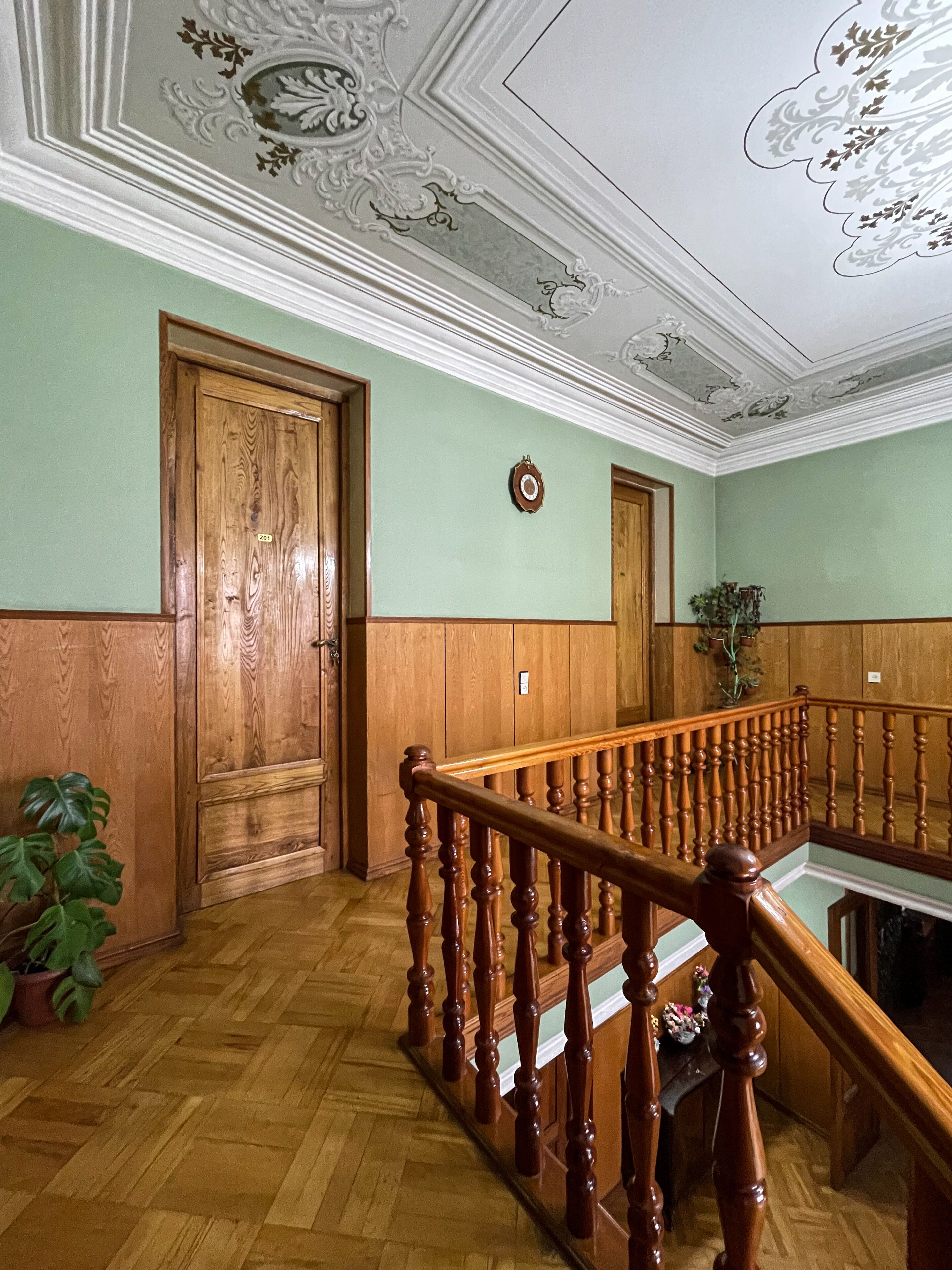 A wooden staircase with a handrail, a green wall with a clock, and a wooden door.