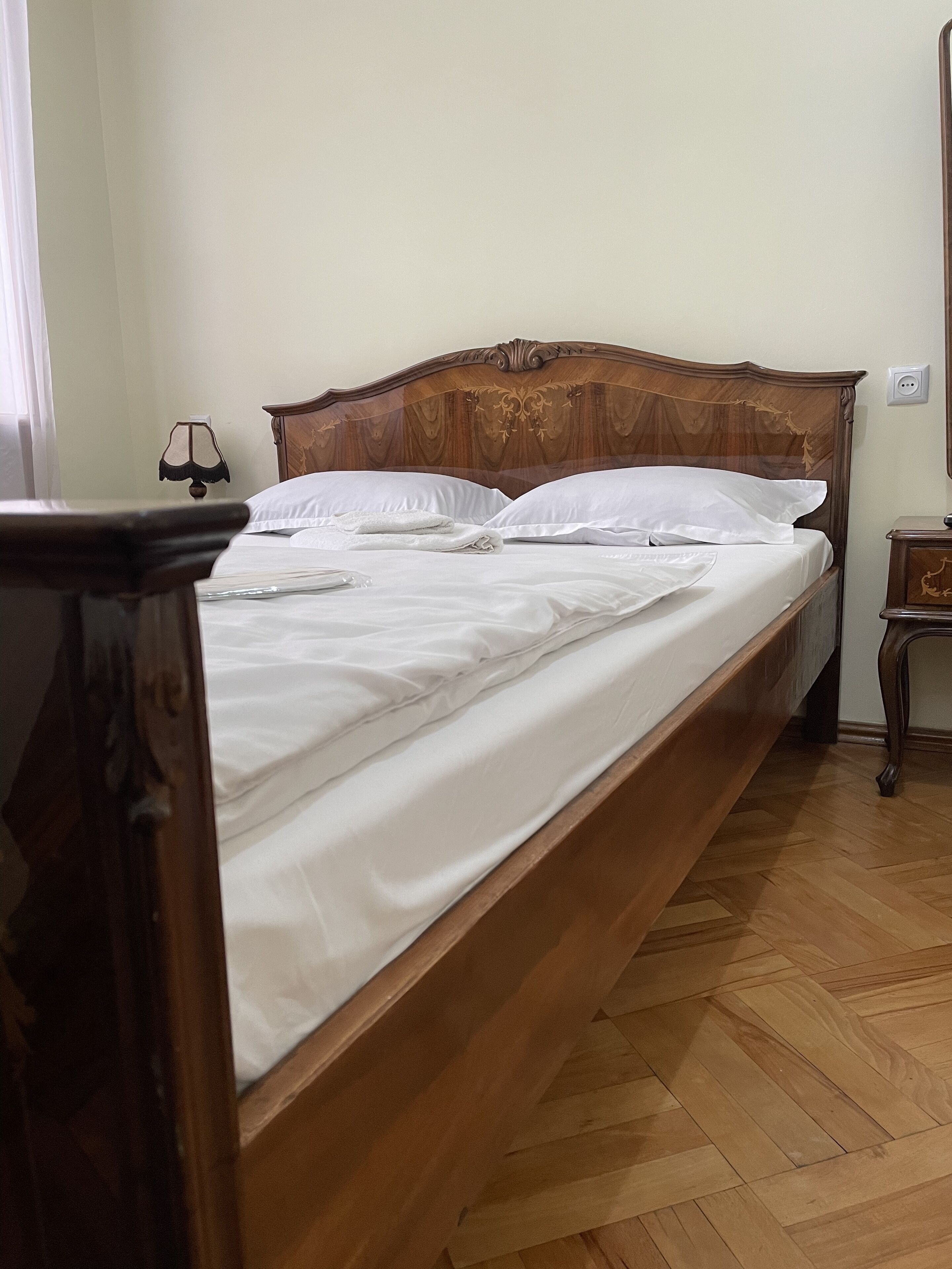 A neatly made bed with white linens in a room with wooden flooring and a wooden headboard.