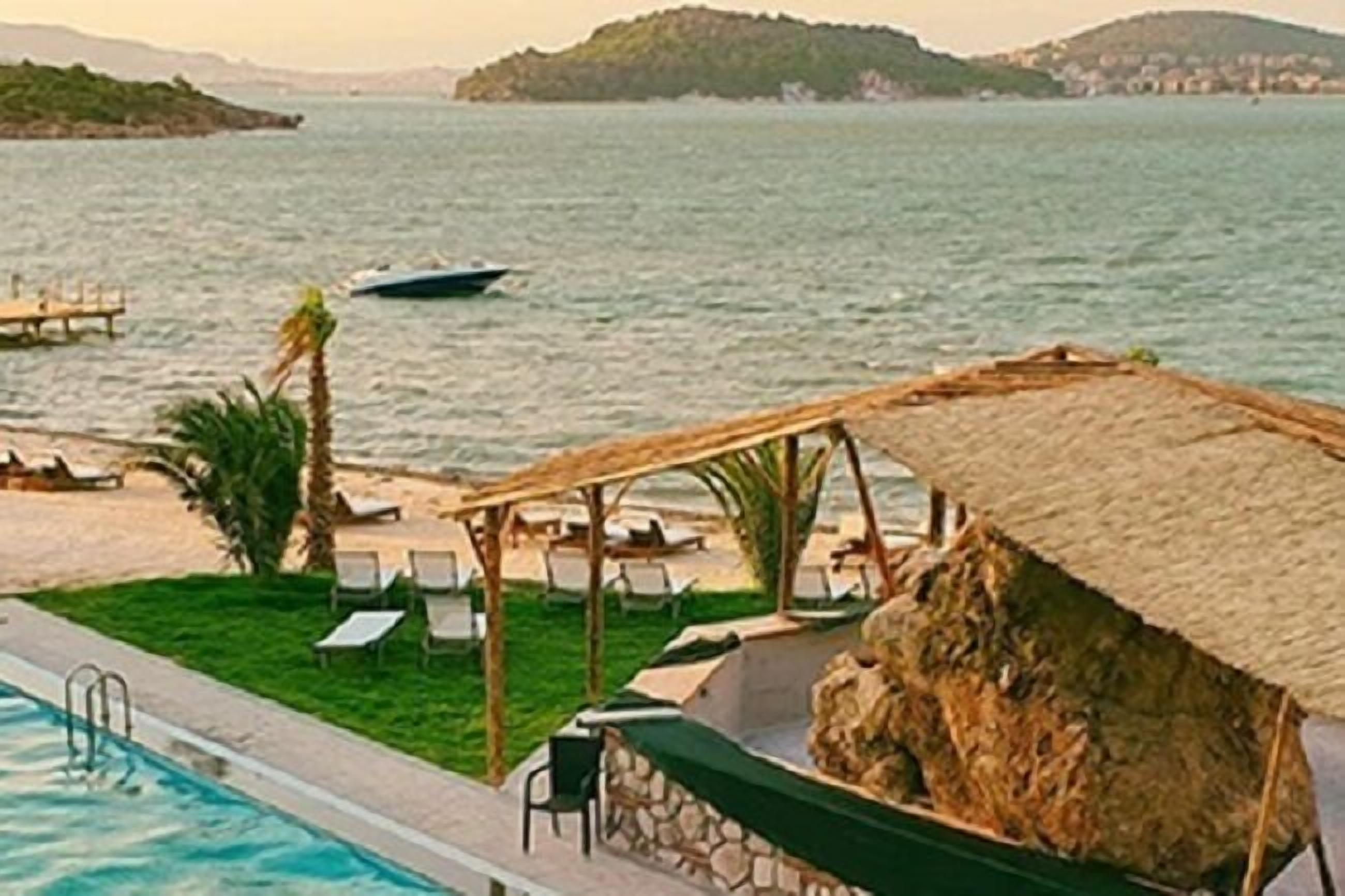 Ein Poolbereich mit Liegestühlen, einem Grill und Blick aufs Meer.