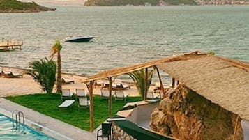 Ein Poolbereich mit Liegestühlen, einem Grill und Blick aufs Meer.