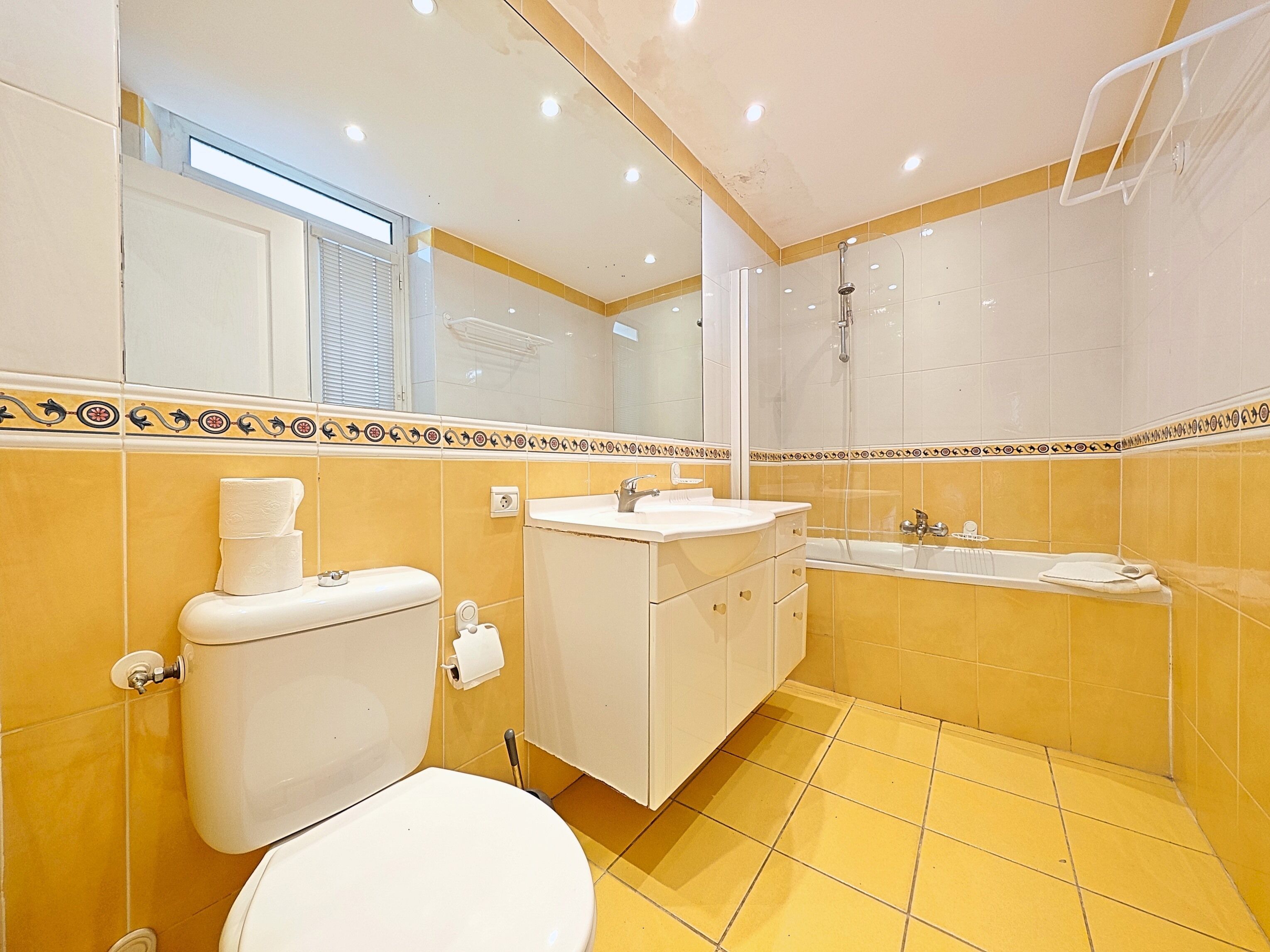 Une salle de bain avec des carreaux jaunes, des toilettes, un lavabo et une baignoire.