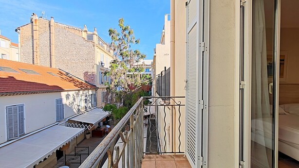 A balcony with a view of adjacent buildings, a table with chairs, and a door leading to a room. - Studio Commandant André 22 by Viva Riviera (Cannes)