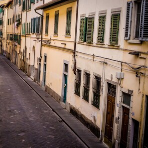 A narrow street lined with buildings featuring traditional architecture, including arched doorways and barred windows. - San Pier Novello in Oltrarno (Florence)