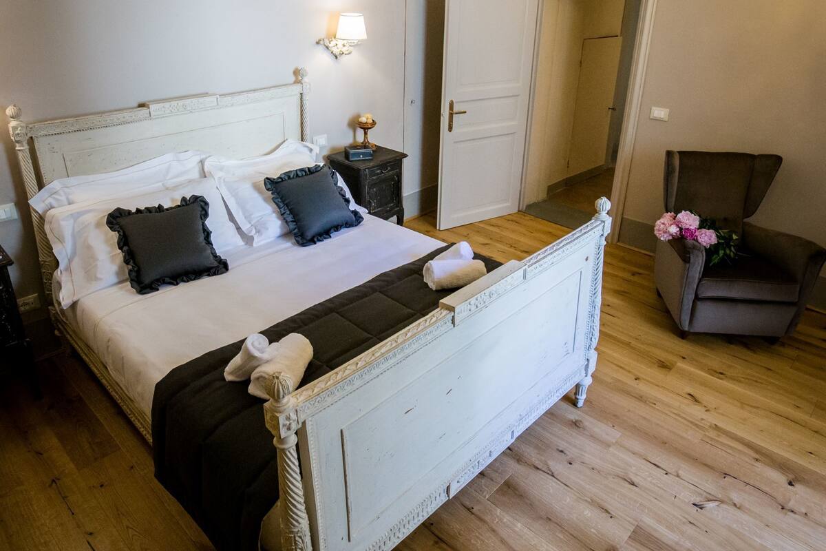A bed with a white headboard, a nightstand with a lamp, and a chair with flowers.