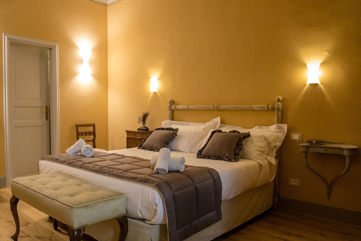 A bedroom with a large bed, a bedside table, a nightstand, and a bench.