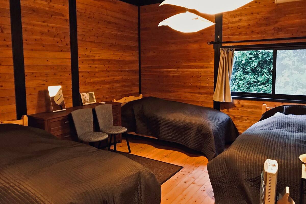 Una habitación acogedora con paredes de madera, un ventanal grande, una cama, una silla y una mesita de noche con una lámpara.