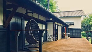 Una terraza de madera con una silla colgante y una mesa, un edificio con techo de tejas y una chimenea.