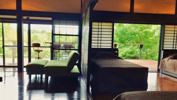 Una habitación amplia con un ventanal grande, una cama, una silla verde y una mesita.