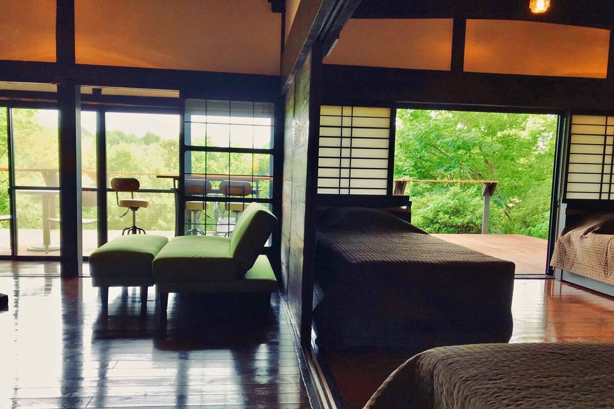 Una habitación amplia con un ventanal grande, una cama, una silla verde y una mesita.