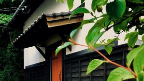 Un edificio de estilo japonés tradicional con una escalera de madera que conduce a una puerta naranja, rodeado de follaje.