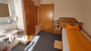 A hotel room with a bed, a bedside table, a mirror, a sink, and a door. - Single room 2 - Gasthaus Zum Spälterwald (Oberzent)