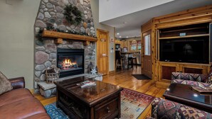 A cozy living room with a stone fireplace, wooden furniture, and a television.
