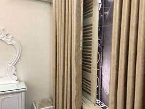 Een kamer met een witte kast, beige gordijnen en een raam met zonwering.