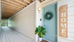 A wooden porch with a light blue door, a welcome mat, and a 'Welcome to Our Home' sign.