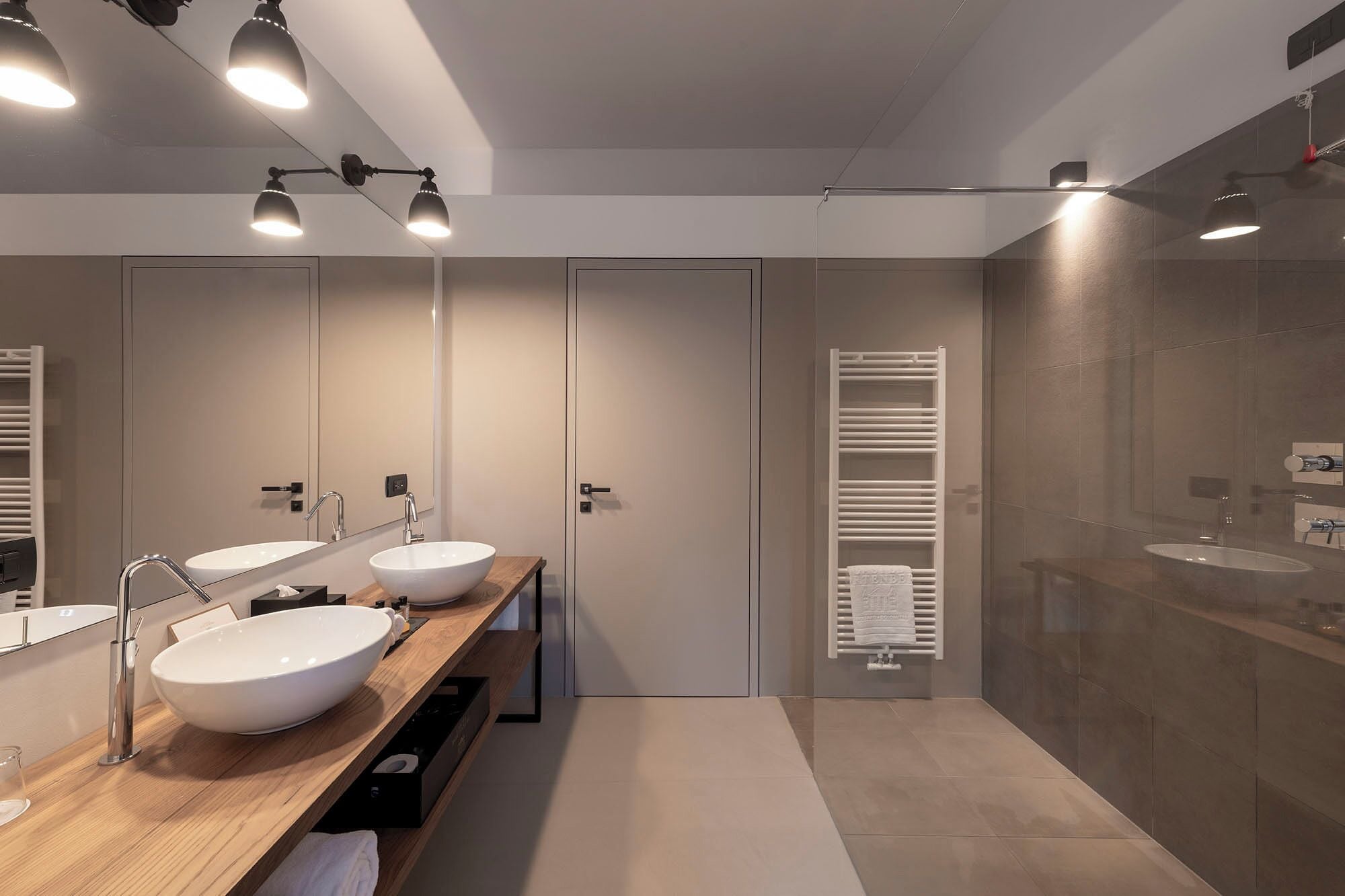 A modern bathroom with two sinks, a large mirror, and a walk-in shower.
