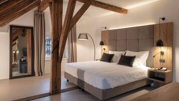 A modern bedroom with a large bed, wooden beams, a nightstand with a lamp, and a view of the city through a window.