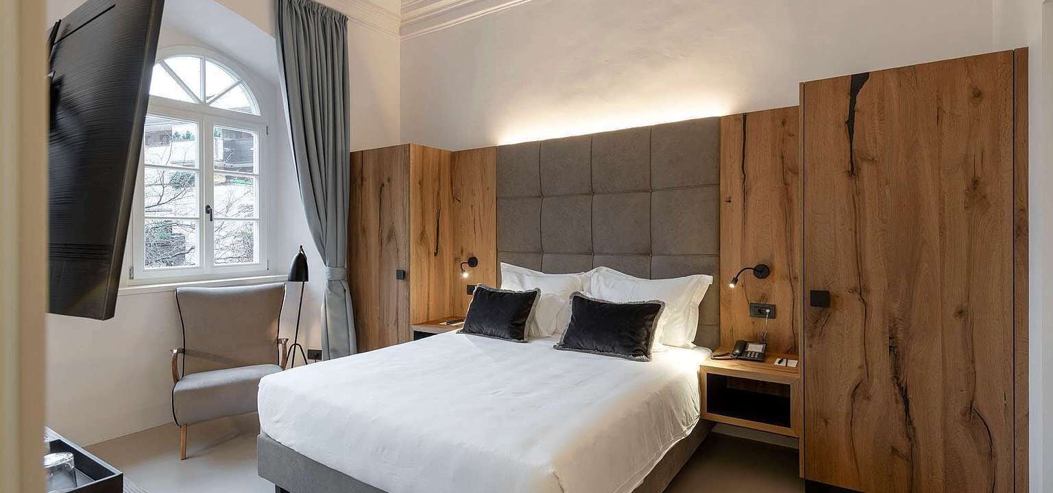 Ein modernes Schlafzimmer mit einem großen Bett, Holzvertäfelung, einem an der Wand montierten Fernseher und einem Fenster mit Vorhängen.