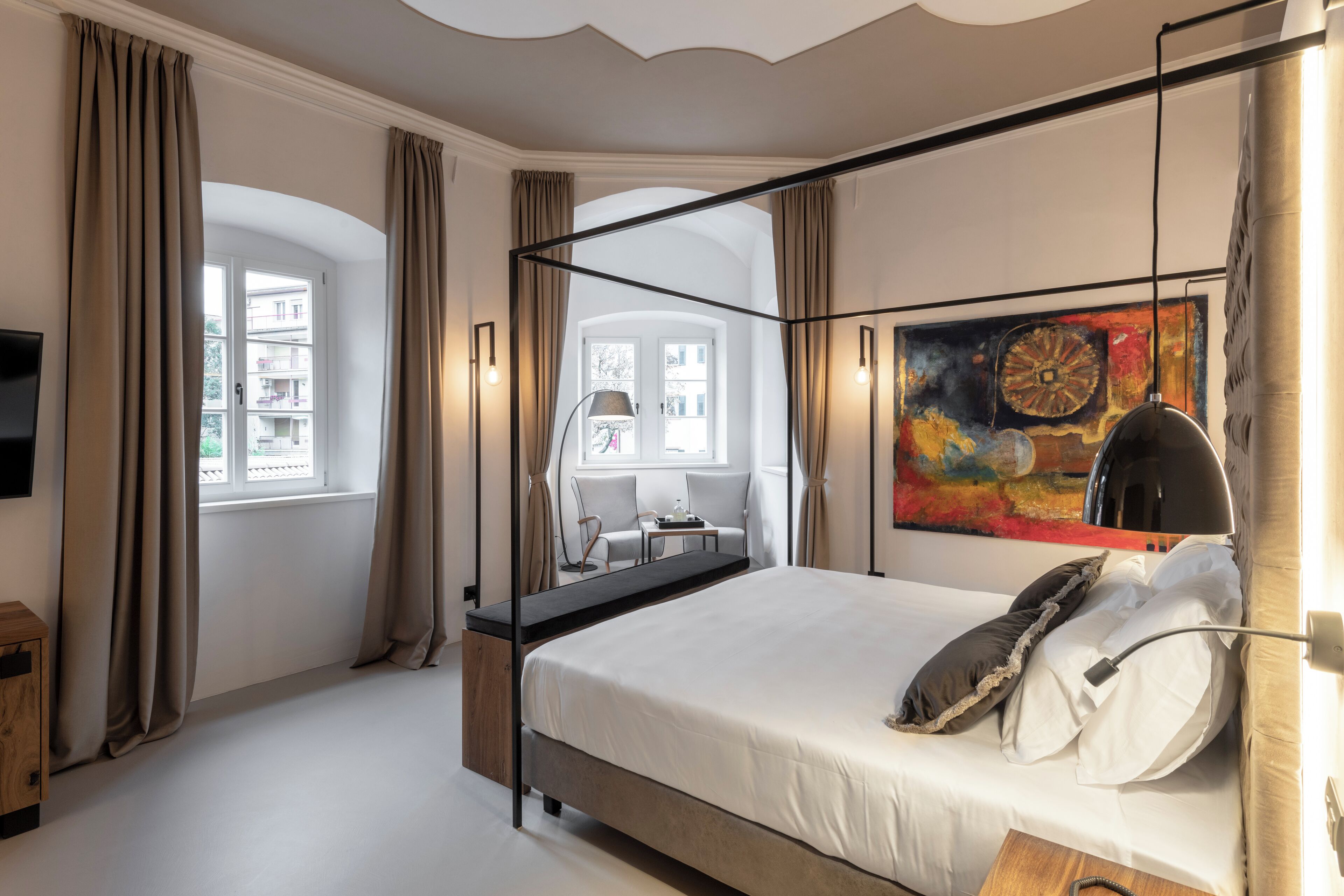 A modern bedroom with a large bed, a desk, a chair, and a painting on the wall.