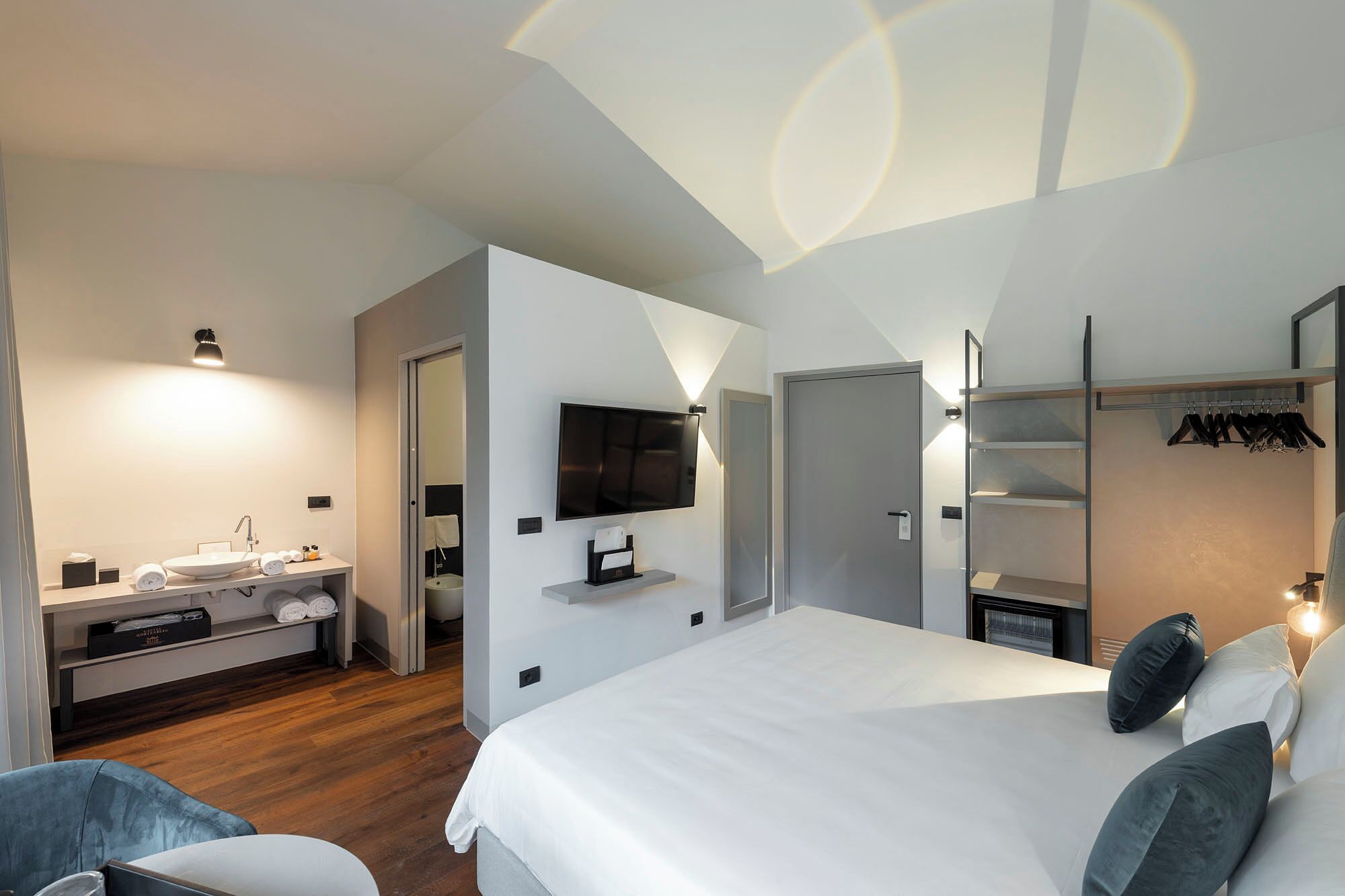 Una camera d'albergo moderna con un letto grande, una televisione, un mobile toilette con lavandino e un armadio pieno di vestiti.