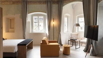 A hotel room with a bed, sofa, ottoman, TV, and a painting on easels.