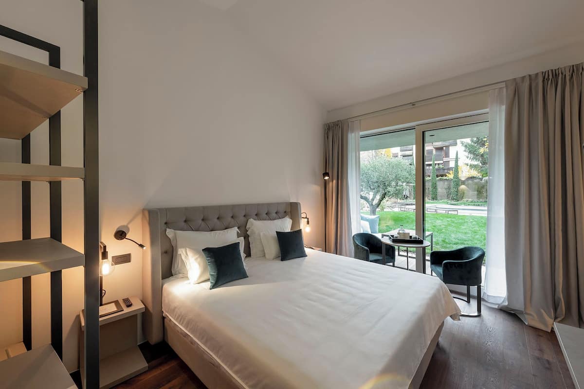 Una habitación de hotel moderna con una cama grande, un escritorio y una silla. Hay una ventana con cortinas y vistas al exterior.