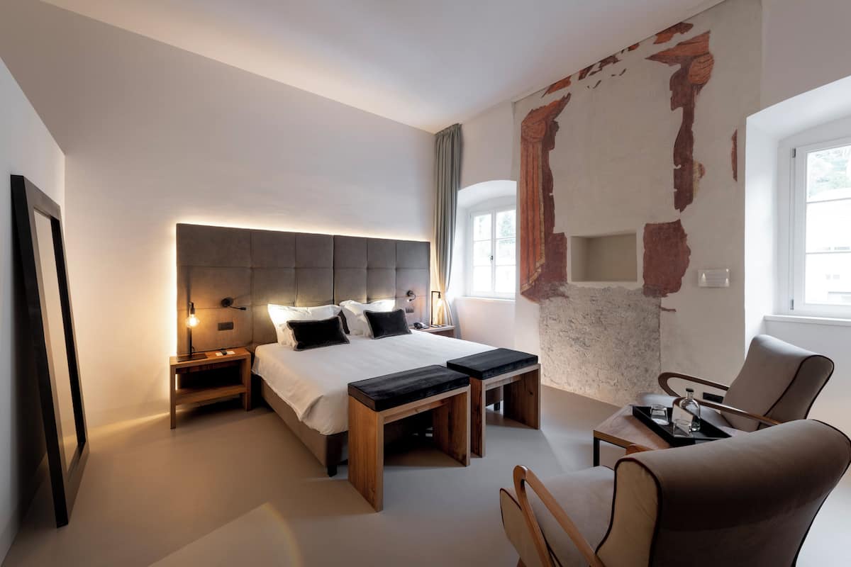 Un dormitorio moderno con una cama grande, mesitas de noche, una silla y un elemento decorativo único en la pared.