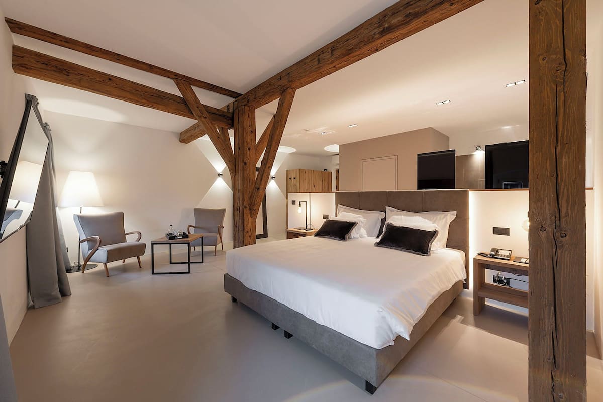 Un dormitorio moderno con una cama grande, vigas de madera, un escritorio y una silla.