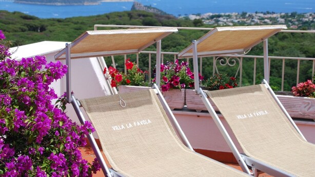 Two sun loungers with "VILLA LA FAVOLA" on the backrest, a balcony with potted flowers, and a scenic view of the sea and hills. - Large apartment sleeping 9 can accommodate 2 families (Barano d'Ischia)
