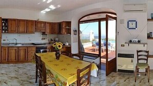 A compact kitchen with wooden cabinets, a dining table with chairs, and a view through a glass door to an outdoor area. - Large apartment sleeping 9 can accommodate 2 families (Barano d'Ischia)